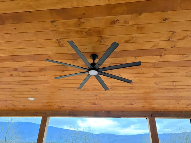 Large black ceiling fan installed on a warm wood porch ceiling